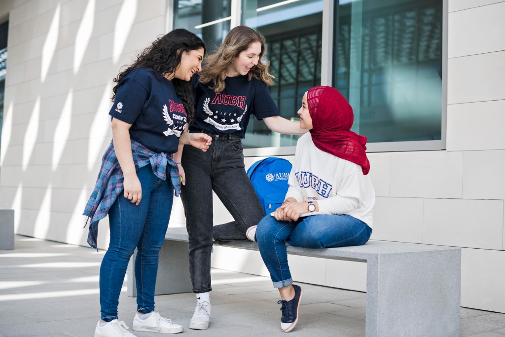 AUBH: three students laughing together outside a campus building, creative direction by Bashar Daas