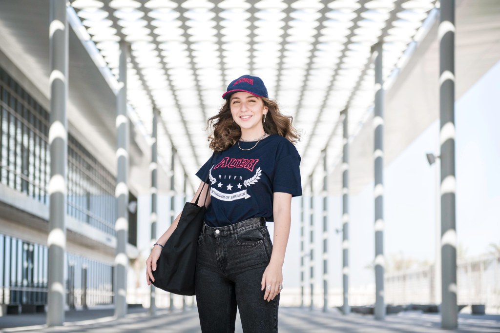 AUBH: a student in an AUBH cap and shirt under the campus colonnade, creative direction by Bashar Daas