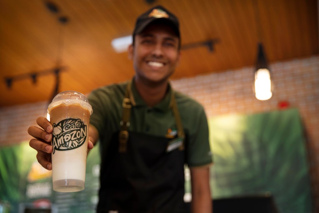 OOMCO: a smiling barista holding up an iced coffee at the station café, creative direction by Bashar Daas