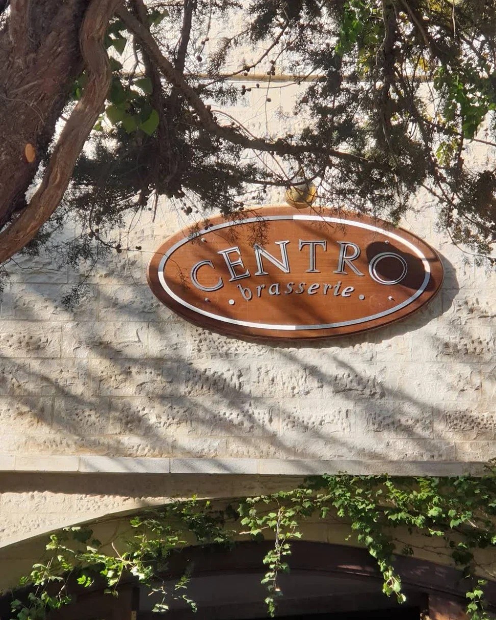 Centro Brasserie: the wooden oval sign on the limestone wall, in the shade of an old tree, creative direction by Bashar Daas