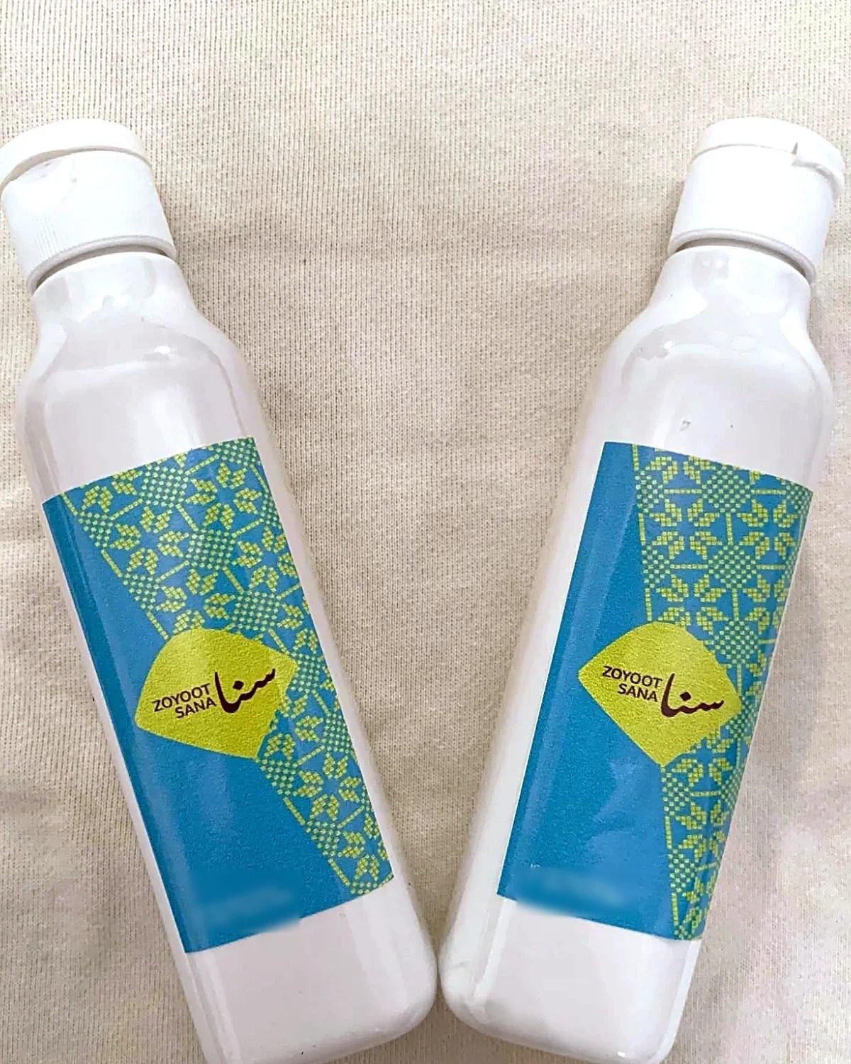 Zoyoot Sana: two white bottles with teal tatreez labels and a lime diamond logo, brand identity by Bashar Daas