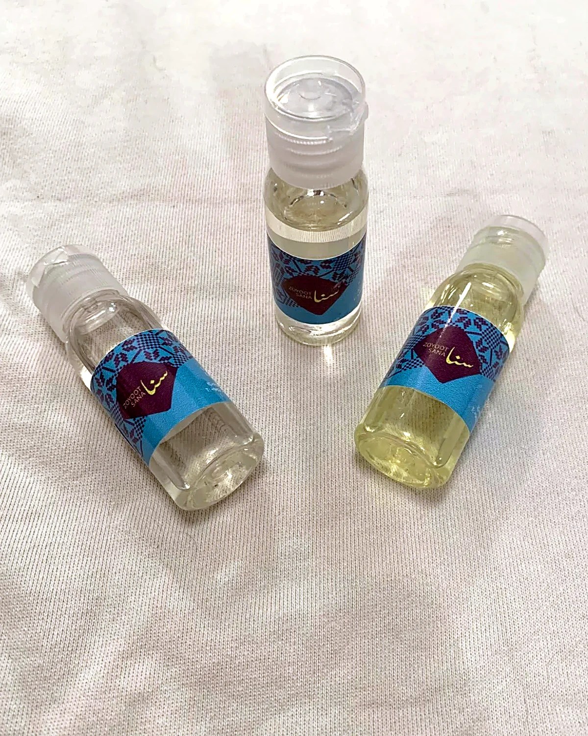 Zoyoot Sana: three small oil bottles with teal tatreez labels and a plum diamond logo, brand identity by Bashar Daas